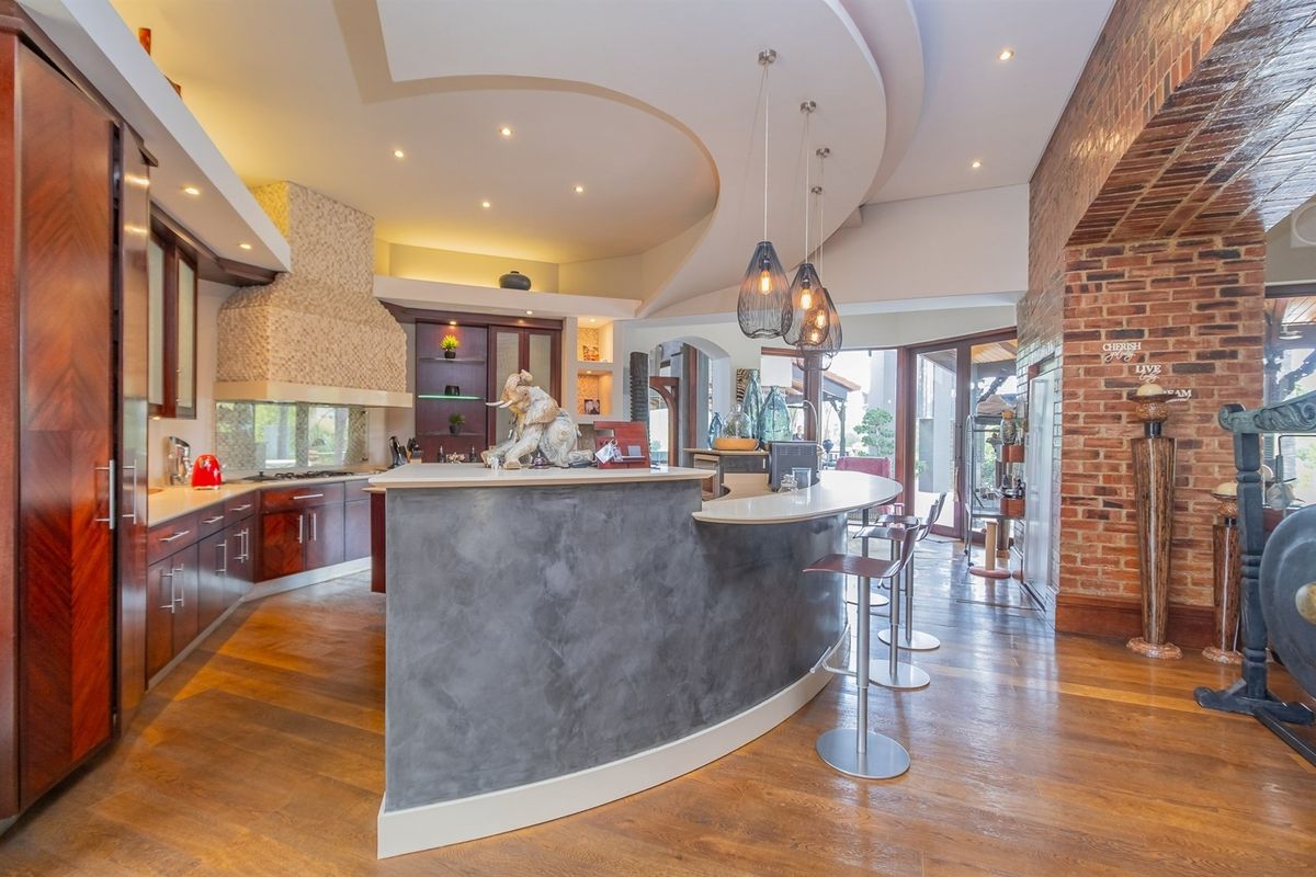 A spacious kitchen featuring a unique curved breakfast bar, custom cabinetry, exposed brick accents, and sophisticated recessed and pendant lighting.