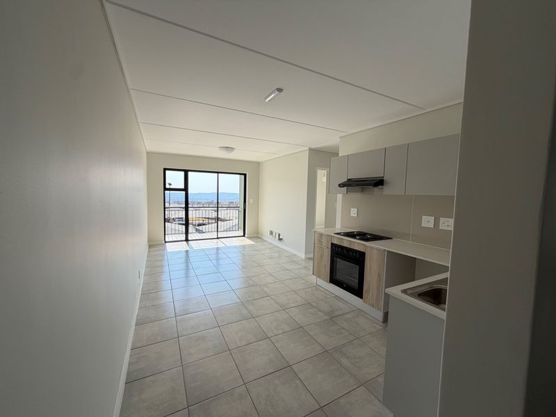 Modern open-plan kitchen and living area featuring tiled floors, built-in cabinetry, integrated appliances, and a sliding door leading to a balcony with views.