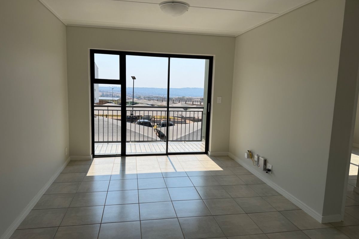 A bright, empty living room featuring neutral tiled flooring and a large sliding glass door that opens onto a balcony with scenic views.