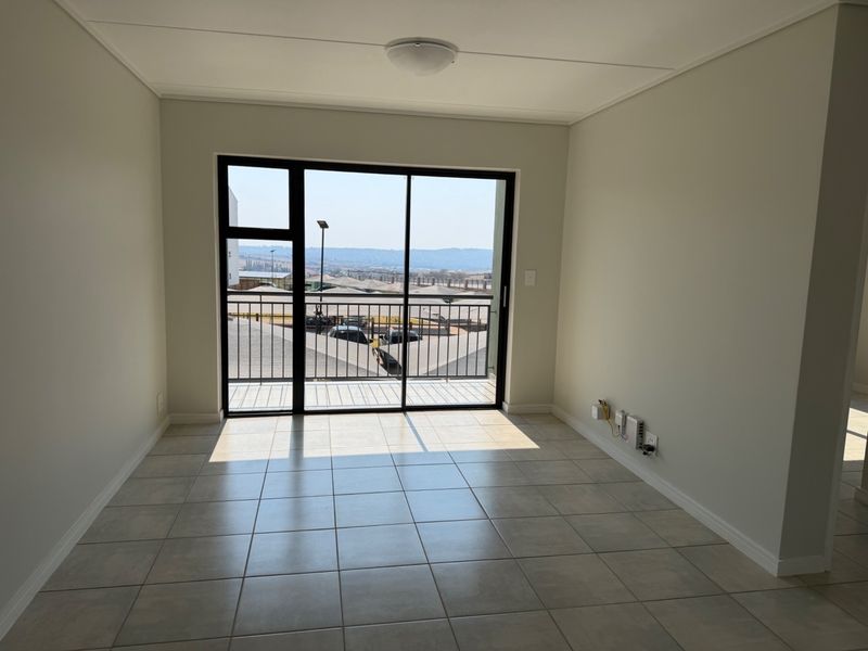 A bright, empty living room featuring neutral tiled flooring and a large sliding glass door that opens onto a balcony with scenic views.