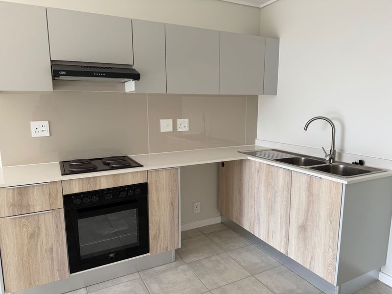 Modern kitchen featuring light wood-grain cabinetry, stone countertops, integrated electric hob and oven, extractor fan, and a stainless steel double sink with mixer tap.