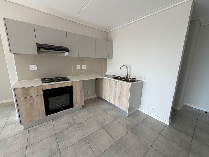 Modern kitchen featuring light wood-finish cabinetry, stone countertops, built-in oven, electric hob, extractor fan, and a double sink with tiled flooring.