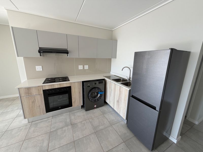 Modern kitchen featuring light wood-grain lower cabinets, grey upper cabinets, glass splashback, built-in oven, electric hob, and tiled flooring.