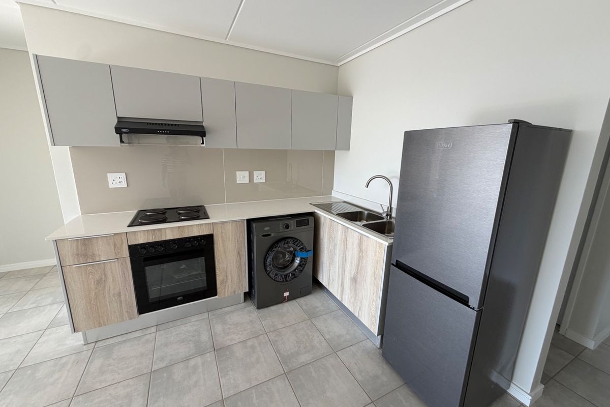 Modern kitchen featuring light wood-grain lower cabinets, grey upper cabinets, glass splashback, built-in oven, electric hob, and tiled flooring.