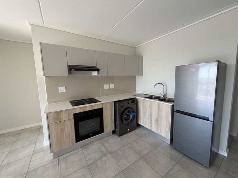 Modern kitchen featuring light wood-finish cabinetry, stone countertops, integrated electric hob and oven, stainless steel sink, and neutral tiled flooring.