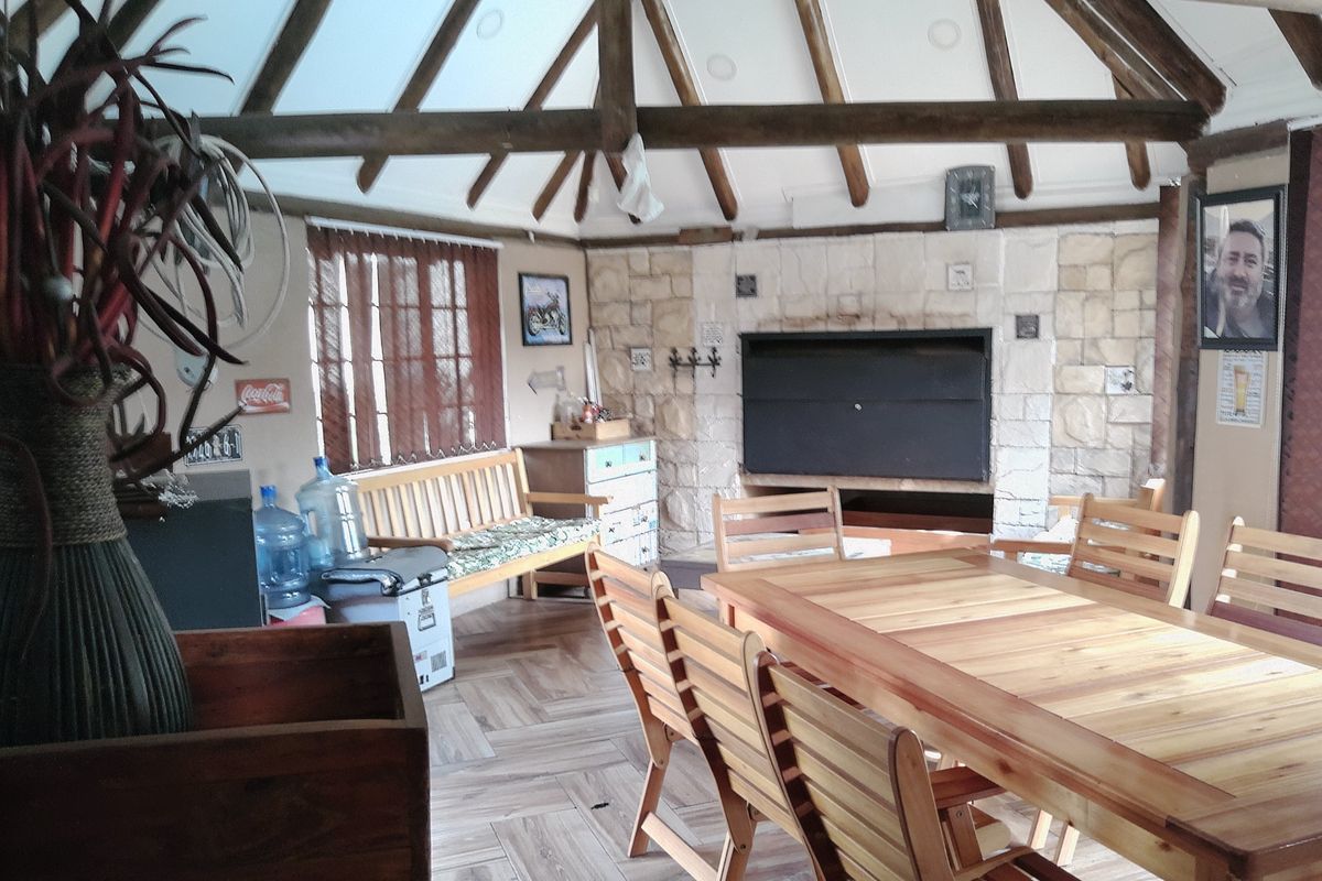 Spacious living area featuring a vaulted ceiling with exposed timber rafters, a stone feature wall with a built-in fireplace, and tiled flooring.
