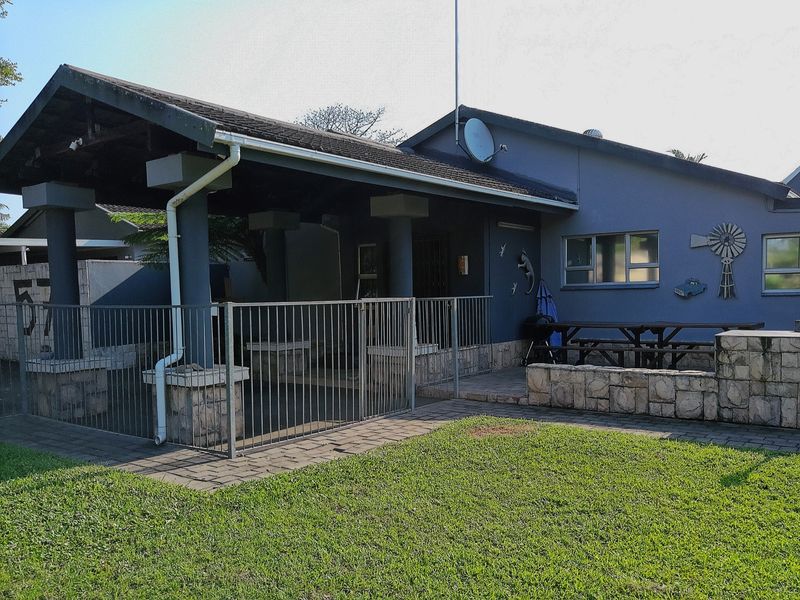 A rear view of the property featuring a covered patio area, stone-clad accents, and a paved walkway leading to a lawn.