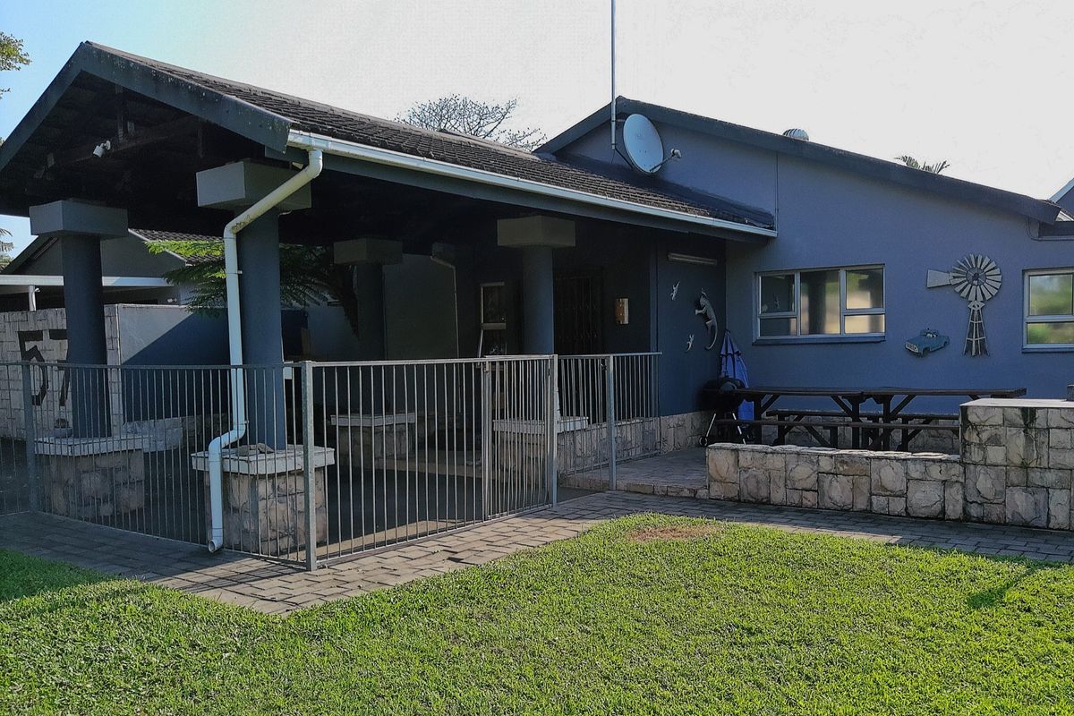 A rear view of the property featuring a covered patio area, stone-clad accents, and a paved walkway leading to a lawn.