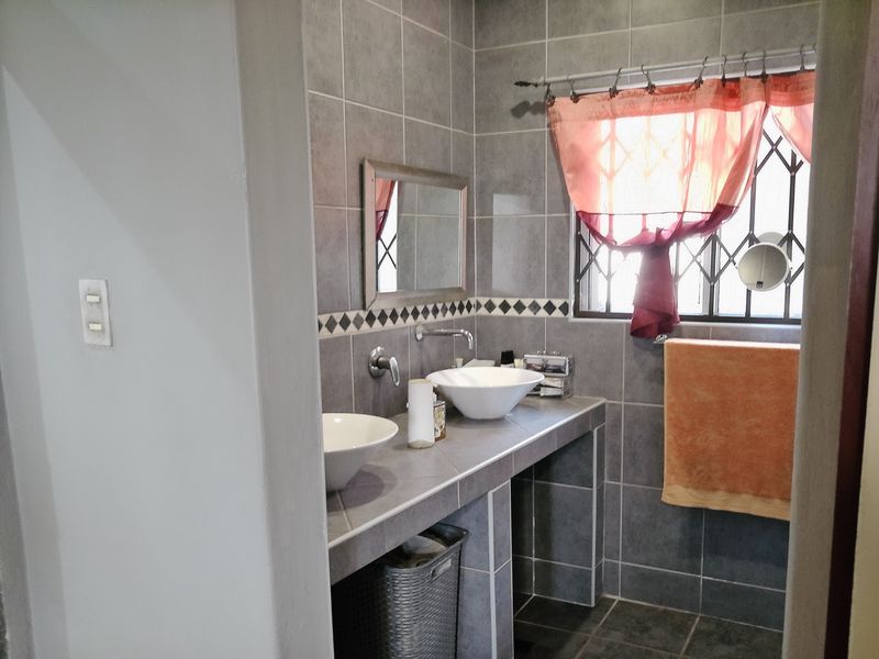 A bathroom featuring a tiled vanity with double vessel sinks, wall-mounted faucets, and full-height wall tiling.