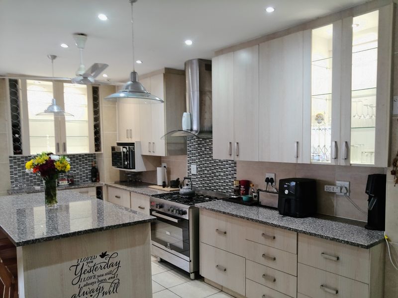 Modern kitchen featuring light wood cabinetry, granite countertops, a central island, stainless steel gas stove, and integrated display cabinets with recessed lighting.