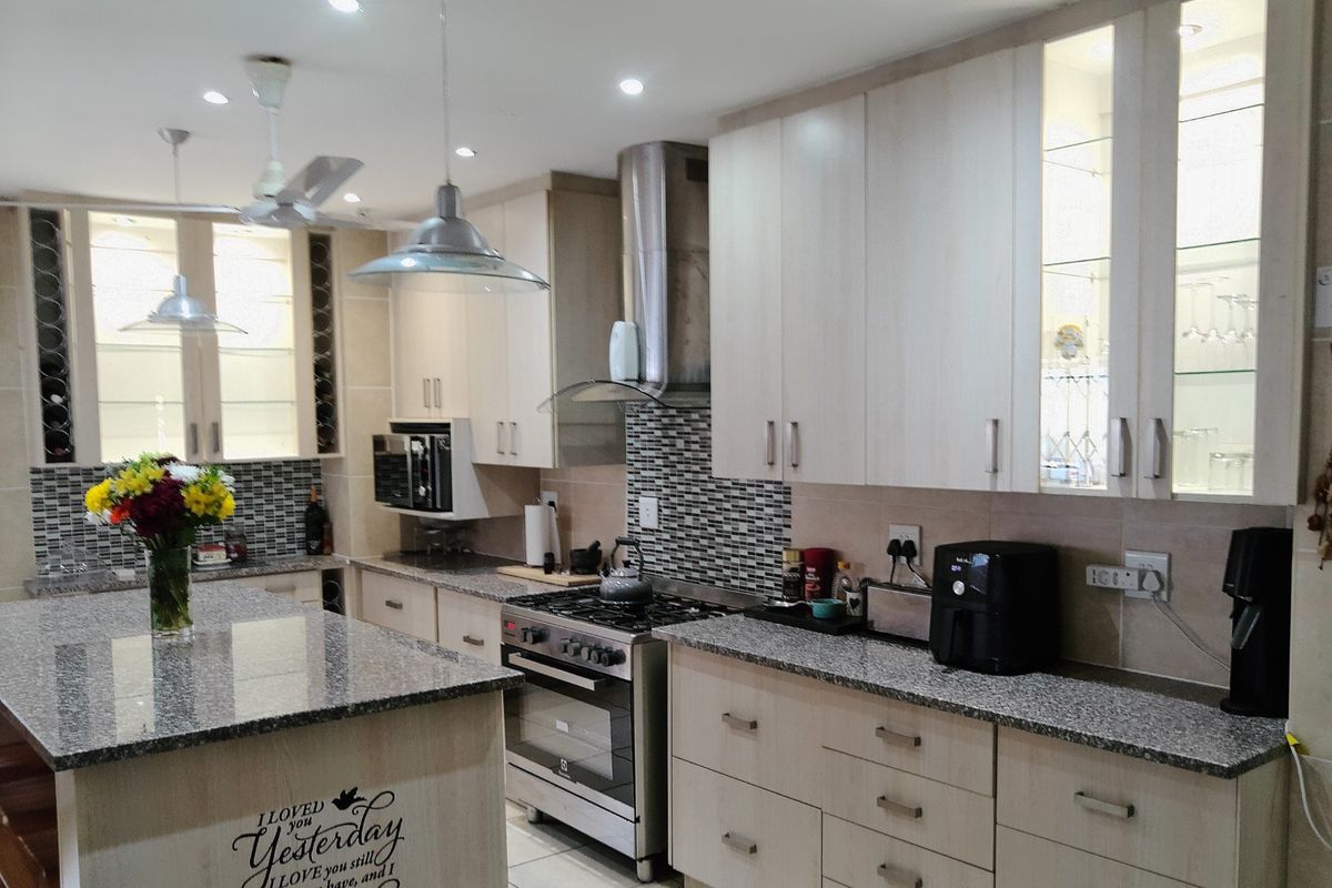 Modern kitchen featuring light wood cabinetry, granite countertops, a central island, stainless steel gas stove, and integrated display cabinets with recessed lighting.