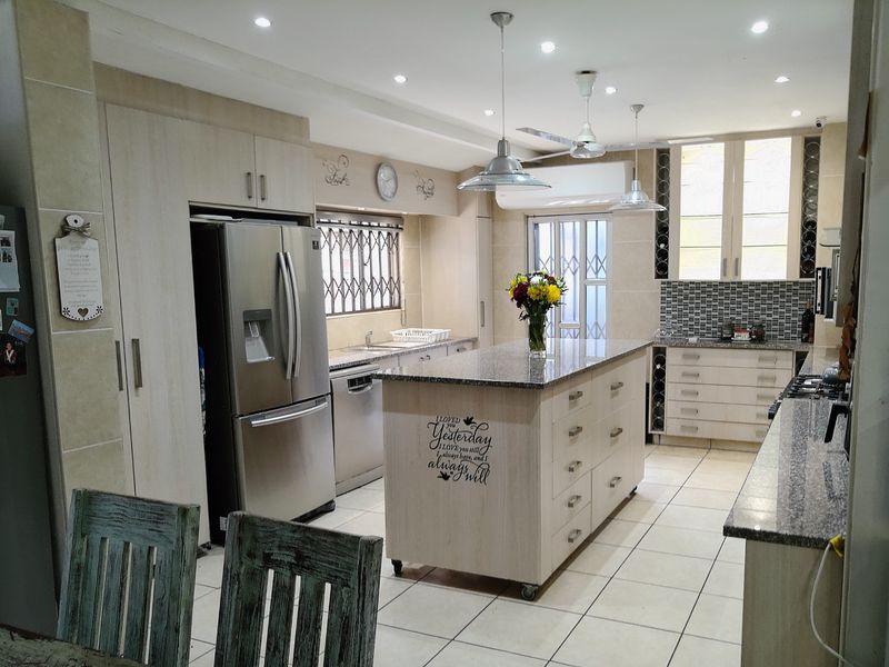 A well-appointed kitchen featuring a central island with granite countertops, extensive built-in cabinetry, mosaic tile backsplash, and modern recessed and pendant lighting.