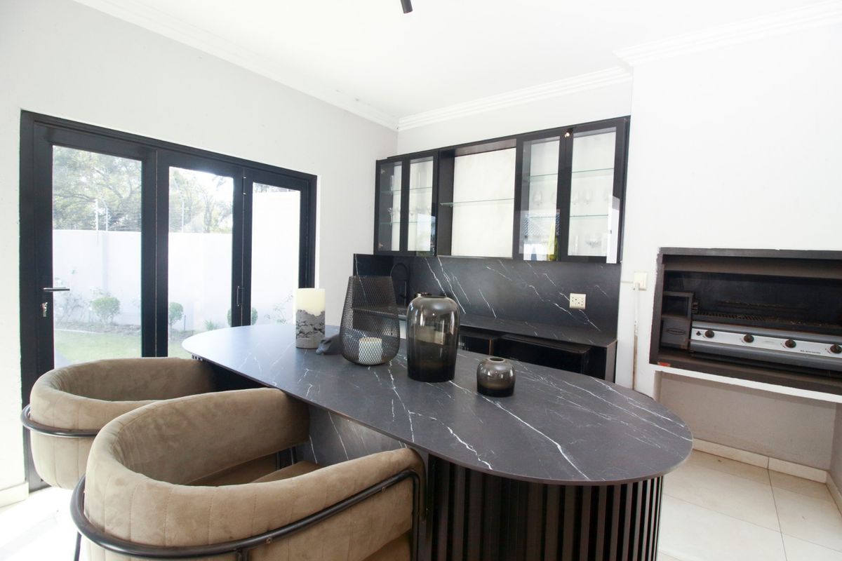 Modern kitchen area featuring sleek black cabinetry, a marble-look island countertop, and a built-in braai, with direct access to the outdoor space.