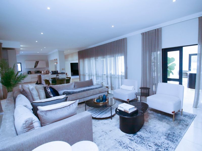 Spacious open-plan living area featuring tiled floors, recessed lighting, and seamless flow to the kitchen and outdoor patio through large sliding glass doors.