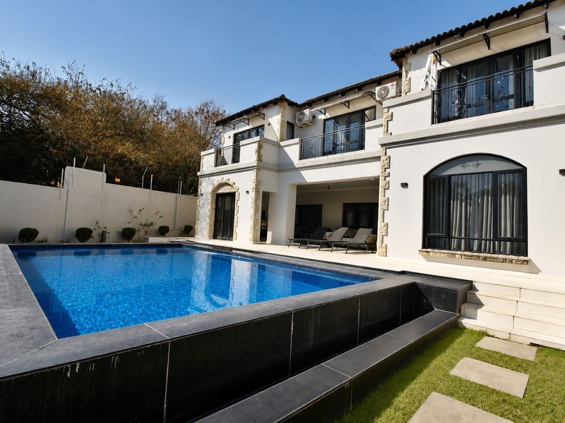 Rear view of a two-story residence featuring a modern swimming pool with dark tiled surround, covered patio, and upper-level balconies.