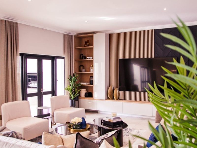 Modern living room featuring custom built-in cabinetry, elegant slatted timber wall paneling, recessed lighting, and large glass doors leading to the exterior.