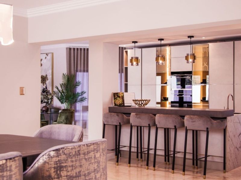 Modern open-plan kitchen and dining area featuring a stone island, mirrored cabinetry, built-in oven, and elegant marble flooring with recessed lighting.