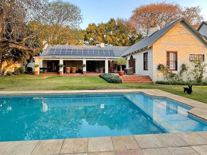 Rear view of a well-maintained house featuring a swimming pool, covered patio, and solar panels set within a landscaped garden.