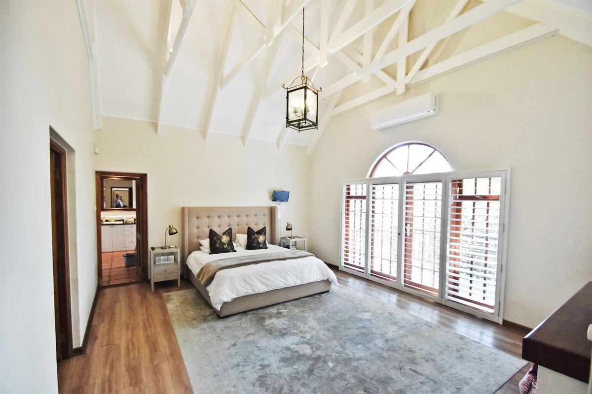 Spacious bedroom featuring a high vaulted ceiling with exposed trusses, arched window with timber shutters, and split-system air conditioning.