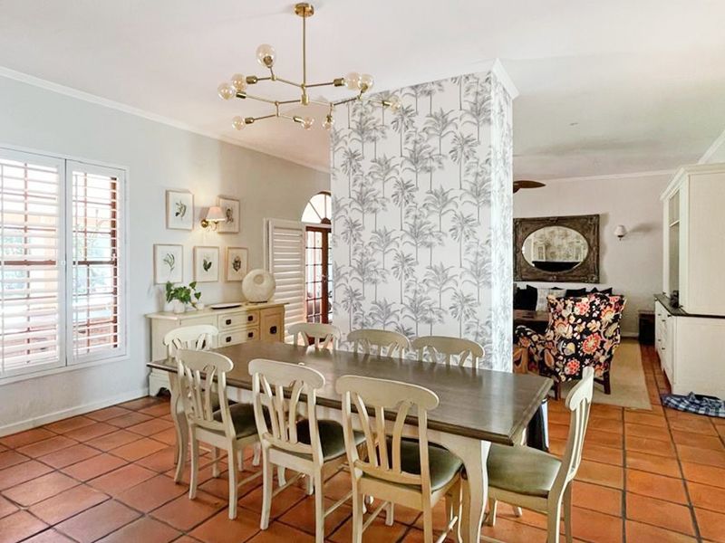Spacious dining area featuring classic terracotta floor tiles, plantation shutters, and a central feature wall with decorative wallpaper.