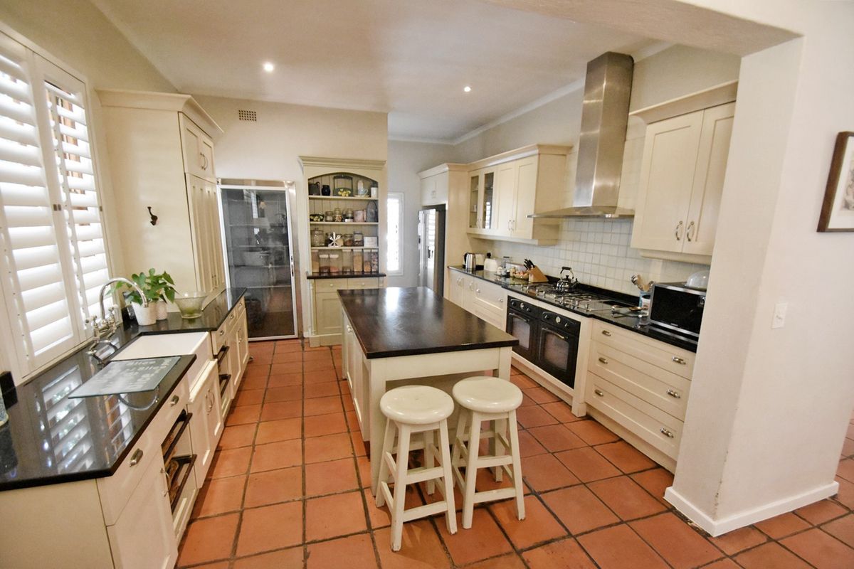 Spacious kitchen featuring shaker-style cabinetry, granite countertops, a central island, farmhouse sink, and high-quality built-in appliances with classic terracotta flooring.