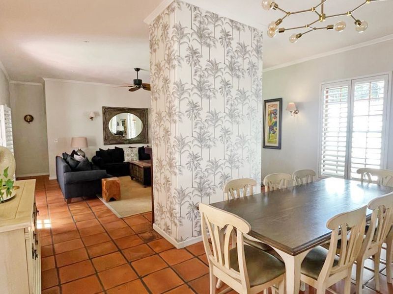 Spacious open-plan living and dining area featuring terracotta floor tiles, a decorative wallpapered feature column, and plantation shutters.