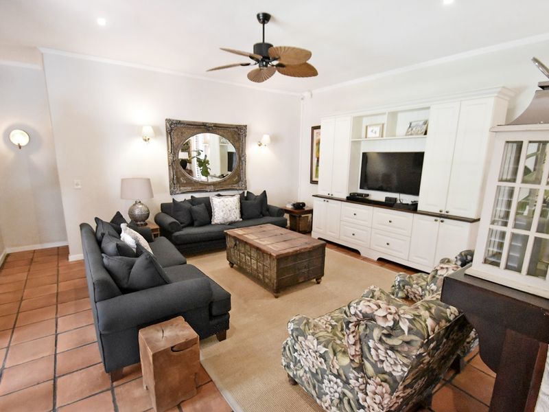 A comfortable living room featuring built-in cabinetry, terracotta floor tiles, and a ceiling fan, providing a warm and functional space for relaxation.