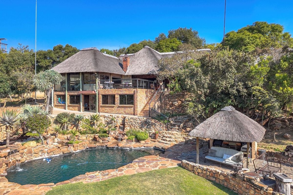 Rear view of a multi-level farmhouse featuring a thatched roof, brick exterior, swimming pool, stone landscaping, and a covered outdoor entertainment lapa.