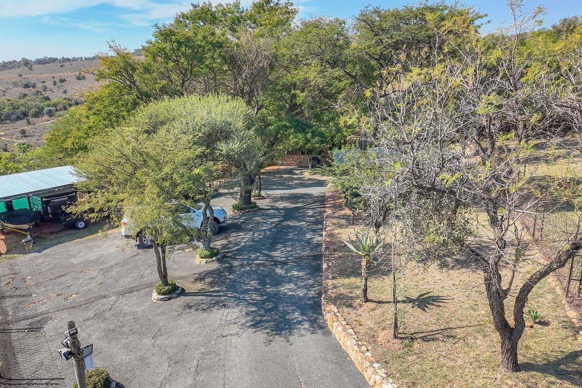 Aerial view of the farm property featuring an asphalt driveway, mature trees, perimeter fencing, and a covered carport area.