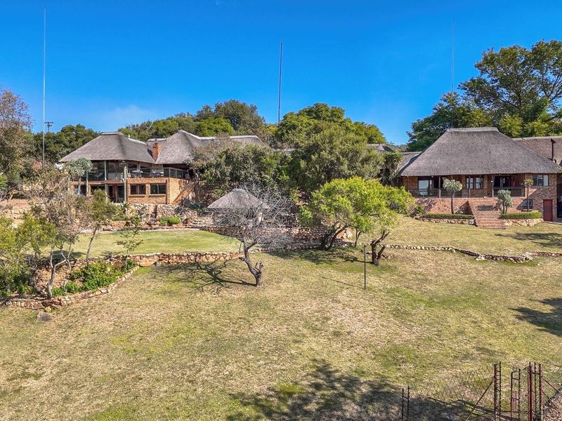 An elevated view of a sprawling farm property featuring multiple buildings with traditional thatched roofs, brick construction, and extensive landscaped garden areas.