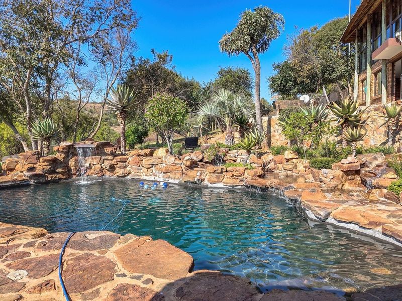 A naturalistic rock-feature swimming pool with a built-in waterfall, set within a landscaped garden area with stone paving and retaining walls.