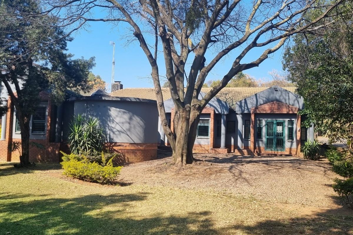 Rear view of a single-story house featuring a combination of brick and painted grey exterior walls, a tiled roof, and mature garden landscaping.