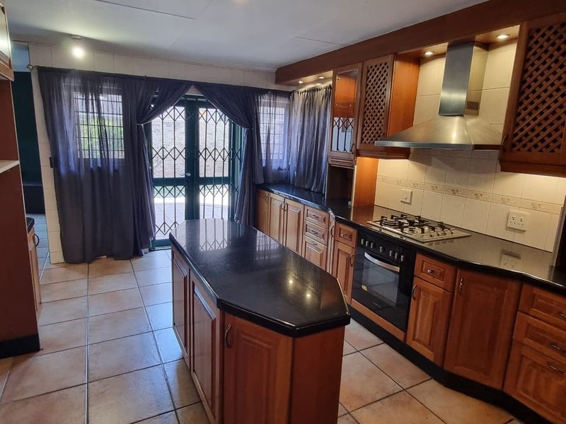 A functional kitchen featuring wooden cabinetry, granite countertops, a central island, and a built-in gas hob with an extractor fan, leading to an outdoor area.