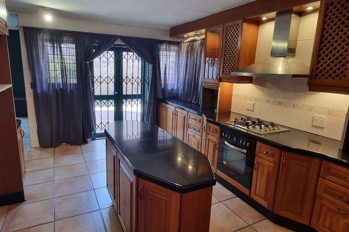 A functional kitchen featuring wooden cabinetry, granite countertops, a central island, and a built-in gas hob with an extractor fan, leading to an outdoor area.