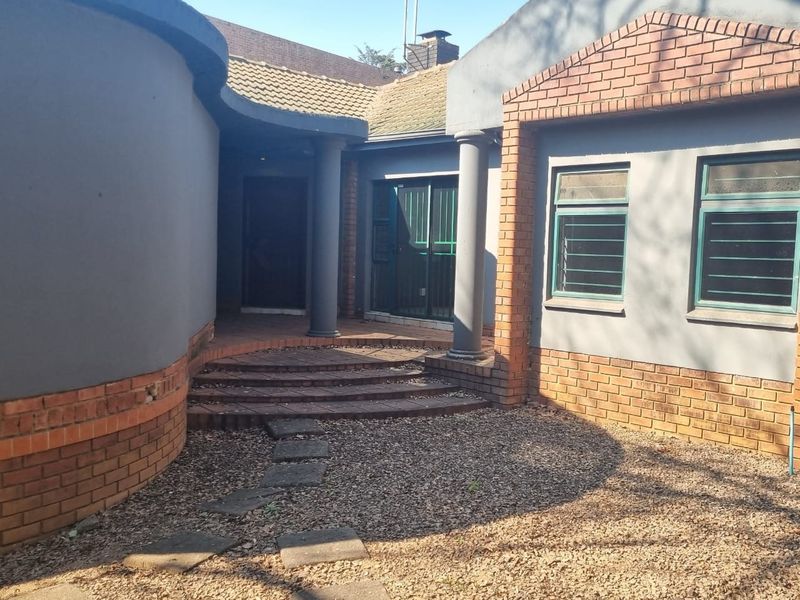 Front entrance area featuring a curved brick wall, stepped tiled porch, and structural columns with security-fitted windows.