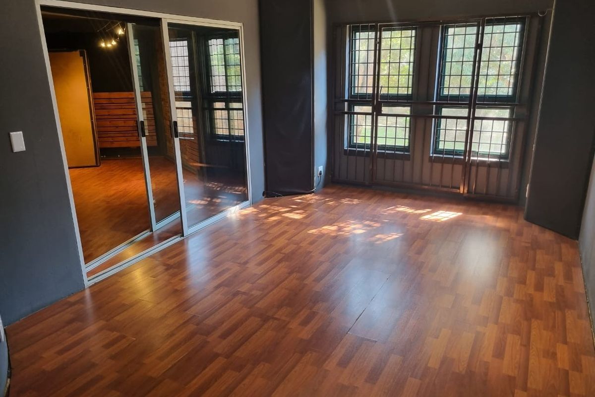 An empty bedroom featuring laminate flooring, sliding mirror wardrobe doors, and windows fitted with security bars.