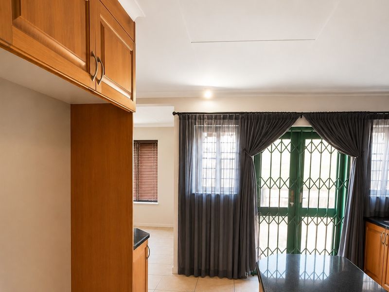 A bright kitchen featuring wooden cabinetry, granite countertops, and tiled flooring, with direct access to the exterior through a secure gate.