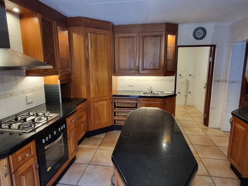 A functional kitchen featuring warm wooden cabinetry, granite countertops, a gas hob, and an integrated oven, with an adjacent utility area visible.