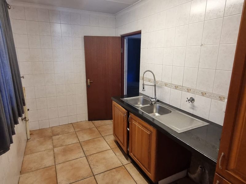 A functional scullery area featuring a double bowl stainless steel sink, tiled splashbacks, and built-in wooden cabinetry with ample counter space.
