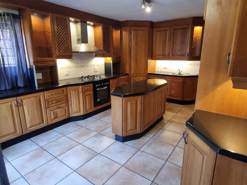 Spacious kitchen featuring traditional wooden cabinetry, black granite countertops, a central island, and integrated appliances with tiled flooring throughout.