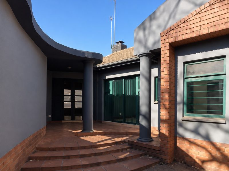 A covered patio area featuring terracotta tiling, structural columns, and a curved roofline, providing access to the home through sliding glass doors.