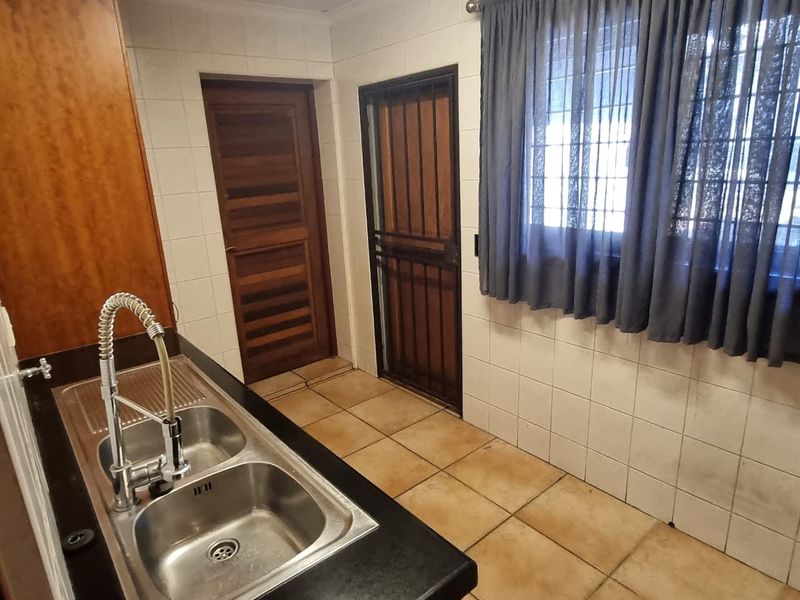 A functional kitchen area featuring a double bowl stainless steel sink, tiled splashbacks, and direct access to the exterior via a security gate.