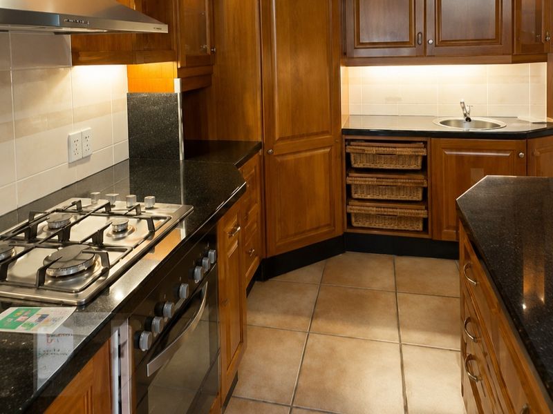 A well-maintained kitchen featuring dark granite countertops, wooden cabinetry, a gas cooktop, built-in oven, and tiled flooring with integrated under-cabinet lighting.