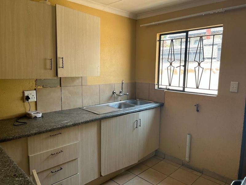 A compact kitchen featuring laminate cabinetry, granite countertops, a stainless steel sink, and tiled flooring, requiring cosmetic updates to improve its overall condition.