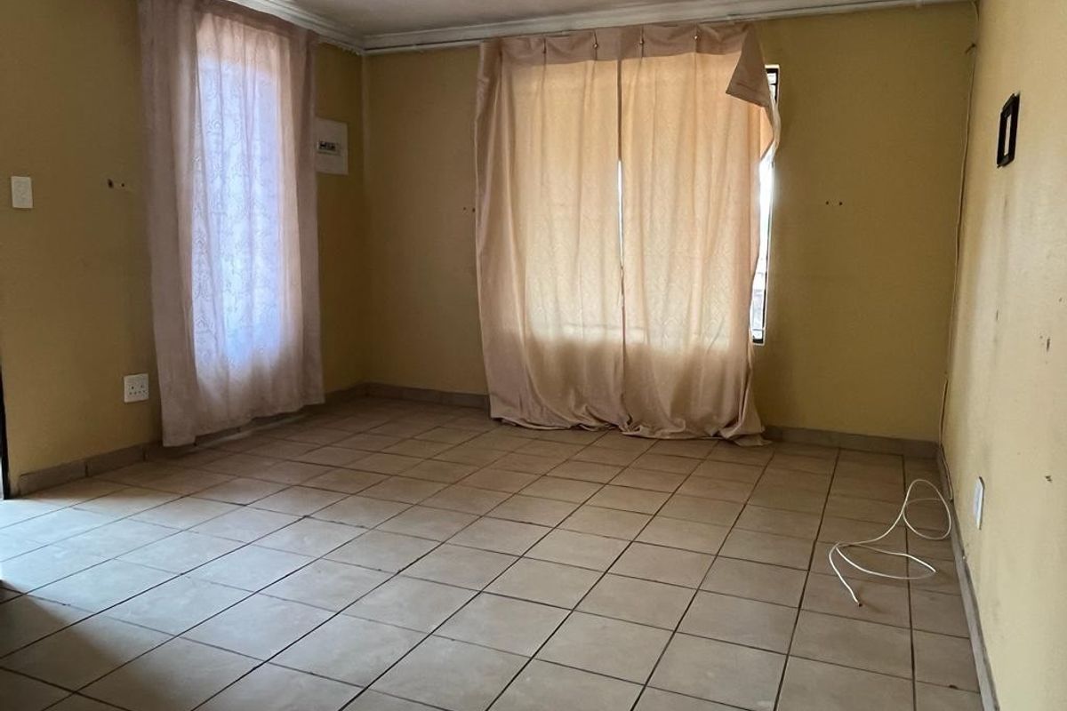 An empty living room featuring ceramic floor tiles and neutral wall finishes, offering a blank canvas for renovation and interior design updates.
