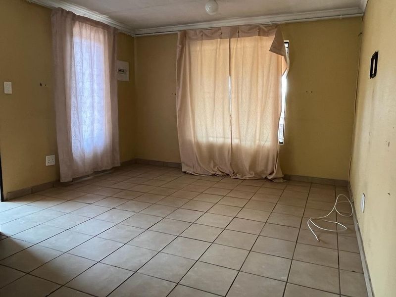 An empty living room featuring ceramic floor tiles and neutral wall finishes, offering a blank canvas for renovation and interior design updates.