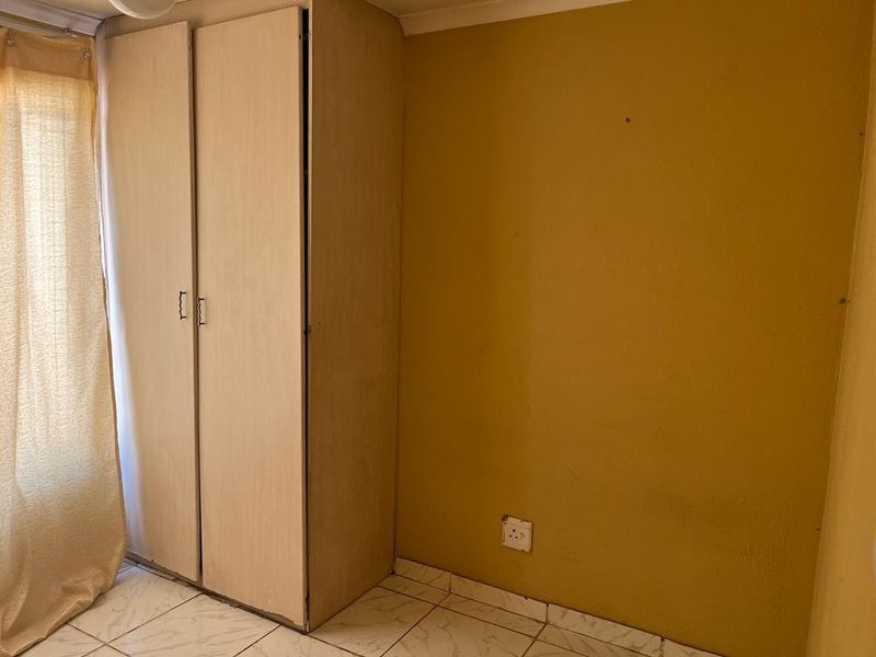 A simple bedroom featuring tiled flooring and a built-in wardrobe, offering a blank canvas for potential updates and interior design improvements.