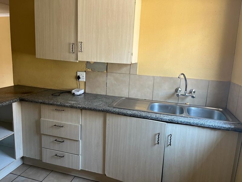 A functional kitchen area featuring laminate cabinetry, a double bowl stainless steel sink, and tiled splashbacks, requiring cosmetic updates to the wall finishes.