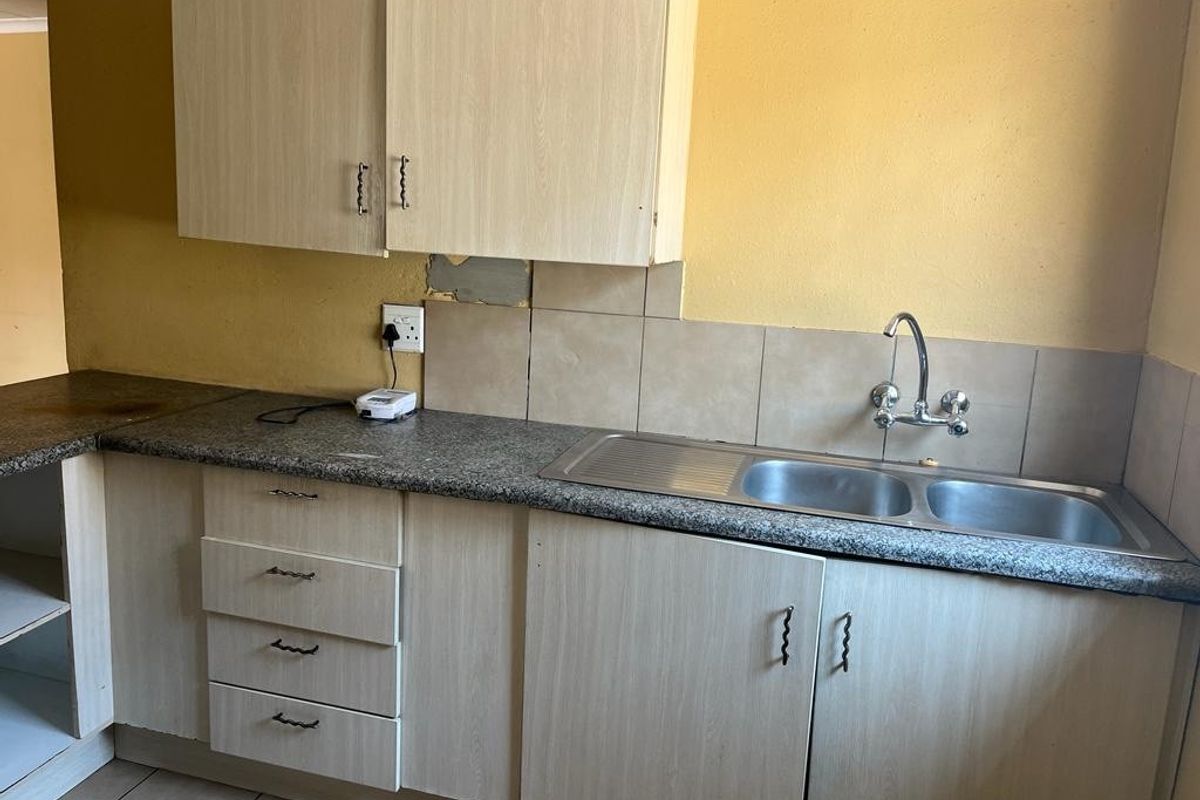 A functional kitchen area featuring laminate cabinetry, a double bowl stainless steel sink, and tiled splashbacks, requiring cosmetic updates to the wall finishes.