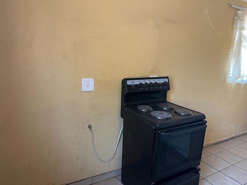 A basic kitchen area featuring tiled flooring and a freestanding stove against a plain wall surface in need of cosmetic attention.